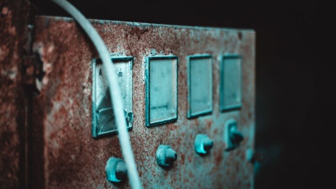 Nærbilde av et rustent elektrisk panel med brytere og kabel