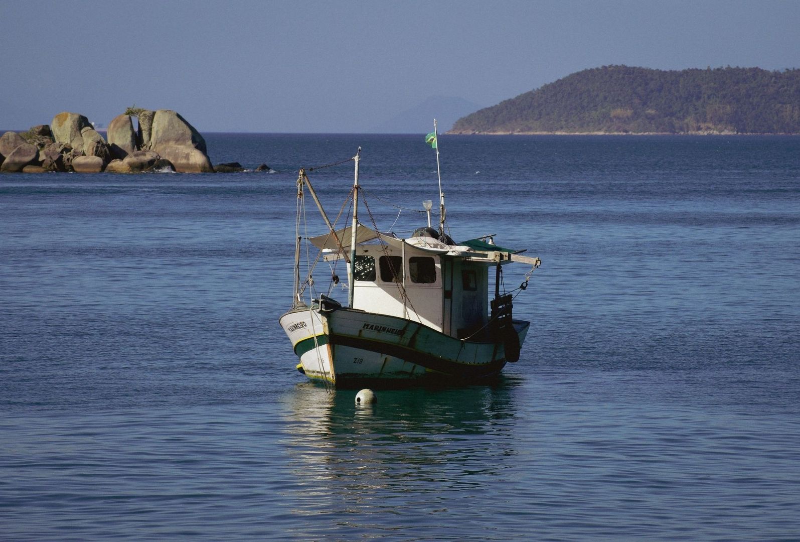 Fiskebåt ligger for anker i rolig farvann ved en holme